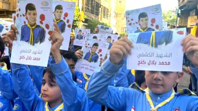 Young lebanese boys in blue shirts and yellow ties hold up paper with colour photocopied images of their school friend who was killed.