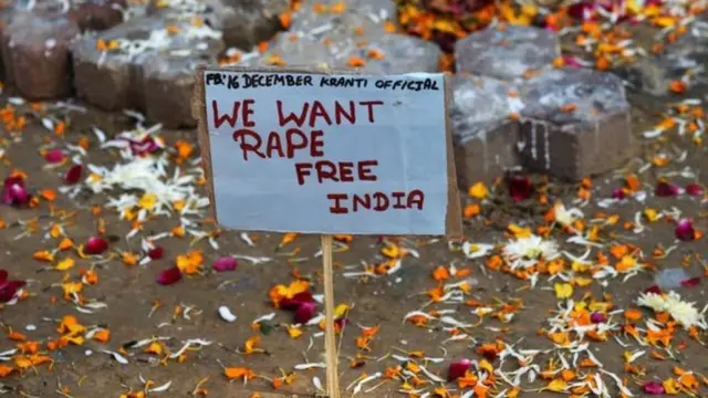 Плакат, на котором написано "Мы хотим Индии - свободной от изнасилованй" на земле среди разбросанных цветочных лепестков