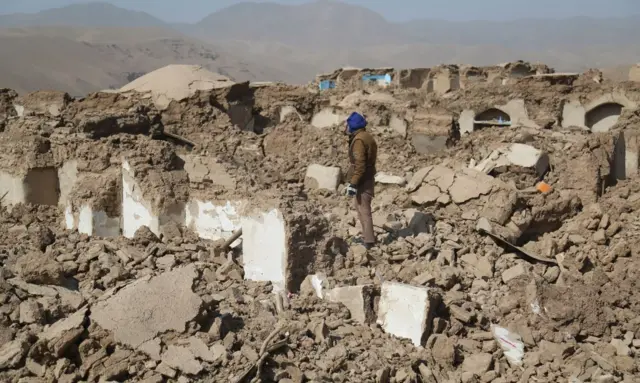 A man stands amidst collapsed homes  