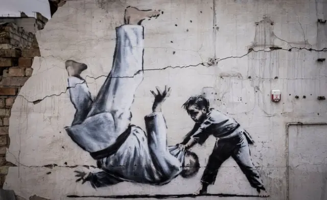 Граффити с изображением мальчик, бросающего мужчину в форме дзюдо, можно увидеть на стене среди разрушенных домов в Бородянке.