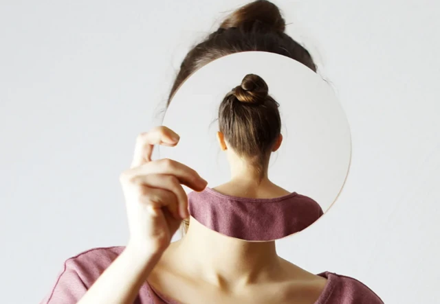 Femme se regardant dans un miroir, qui montre son reflet le dos tourné