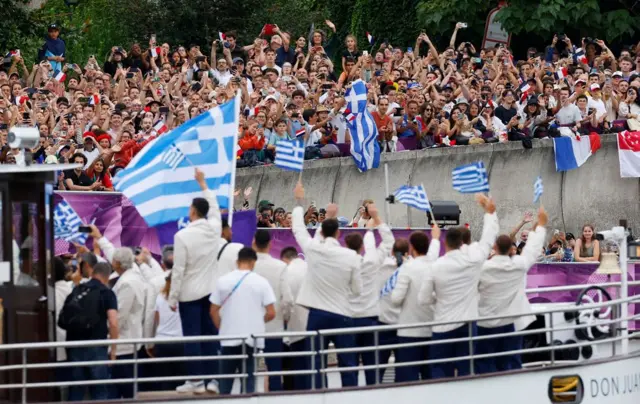 Team Greece wave at cheering spectators from their boat on the River Seine during the opening ceremony