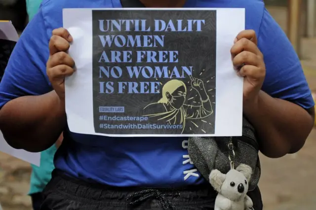 Крупным планом руки, коорые держат плакат против сексуального насилия, направленного на женщин из низжих каст