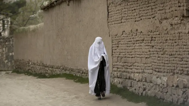 Женщина в парандже на фоне глинобитной стены