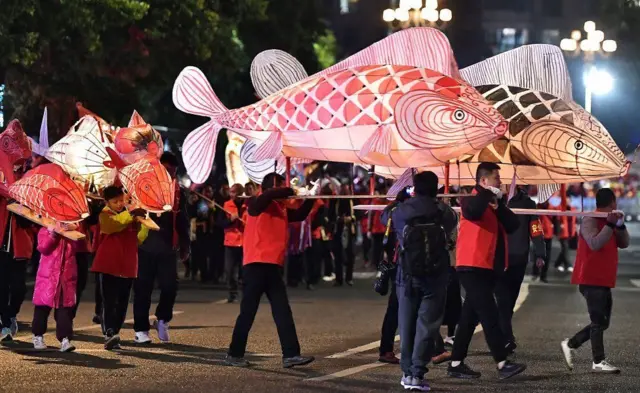 Люди несут большие фонари в виде рыб