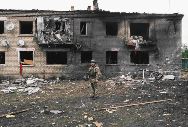Украинский военный на фоне обгоревшего и разрушенного дома
