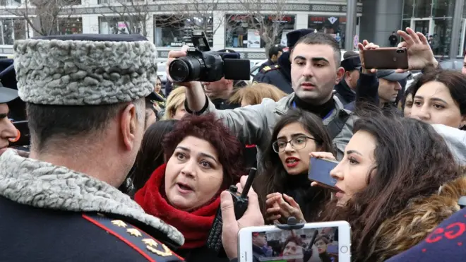 Женщина, полицейский стоящий спиной к камере. Вокруг толпа