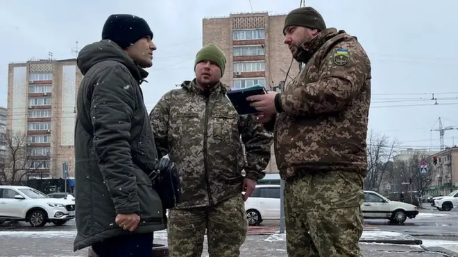 Des officiers de conscription s'adressent à un homme dans une rue de Cherkasy.