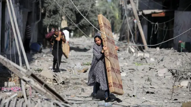 Mulher carrega colchão em meio aos escombros em Gaza