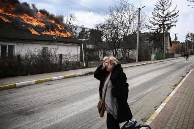 Une femme se couvre le visage avec sa main devant une maison en feu à Irpin, près de Kiev, le 4 mars 2022.