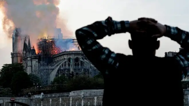 A man watches the landmark Notre-Dame Cathedral burn, engulfed in flames, in central Paris on April 15, 2019