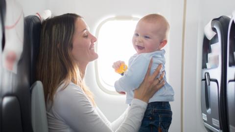 A mother holding her baby in front of her face, smiling, while sat on a plane.