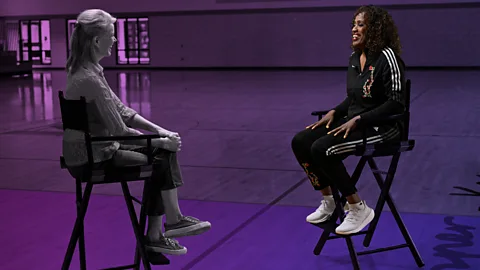BBC/ Scott Rovak Katty Kay and Jackie Joyner-Kersee facing each other on chairs. The image is stylised with a purple wash over it, apart from Joyner-Kersee who is in full colour (Credit: BBC/ Scott Rovak)