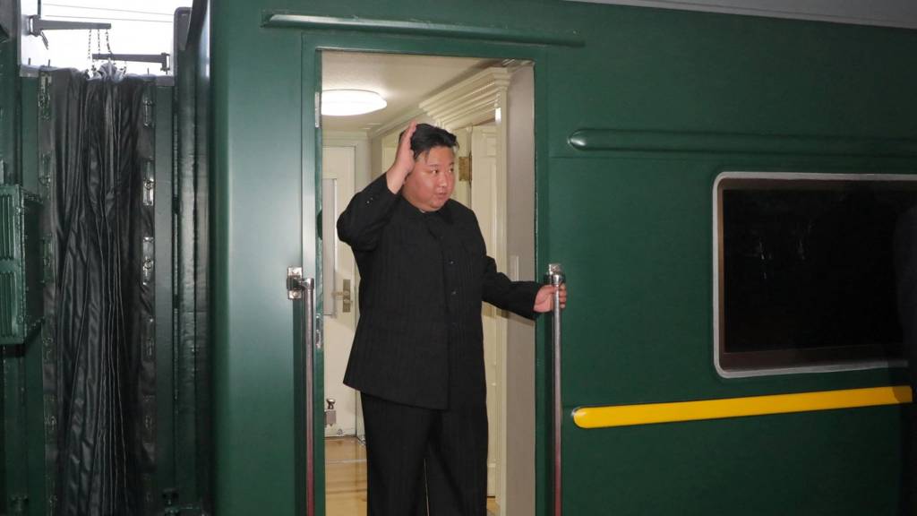 Kim Jong Un waves from a green train as he departs Pyongyang, North Korea