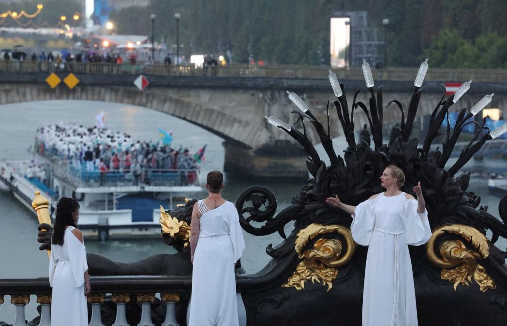 Performers dressed in white robes stand on Pont Alexandre III during the opening ceremony of the Paris 2024 Olympics, as a boat passes beneath