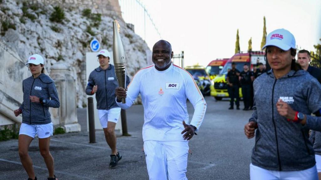 French former football player Basile Boli holds the Olympic Torch as part of the Olympic and Paralympic Torch Relays at the Notre Dame de la Garde Basilica