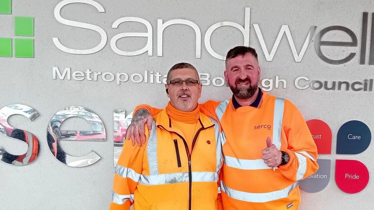 Kevin Marriott (left) and Steve Whitehouse (right) in their work uniforms, in front of a Sandwell Council logo. Mr Whitehouse gives a thumbs up to the camera