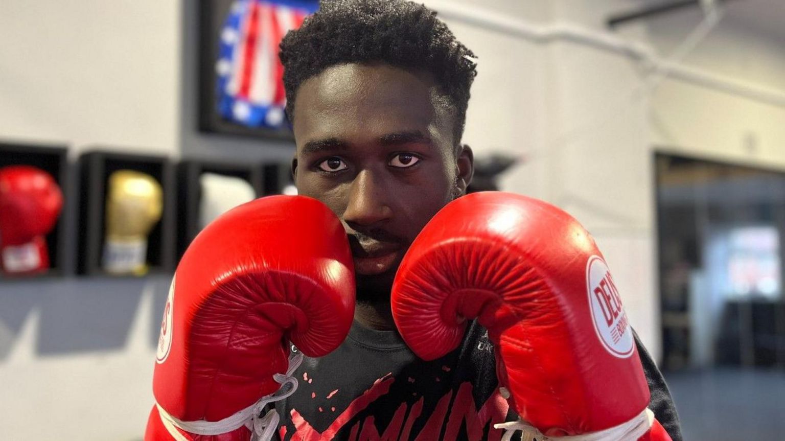 Boxing prospect Adam Olaore holds his red boxing gloves in front of his face in a defensive pose
