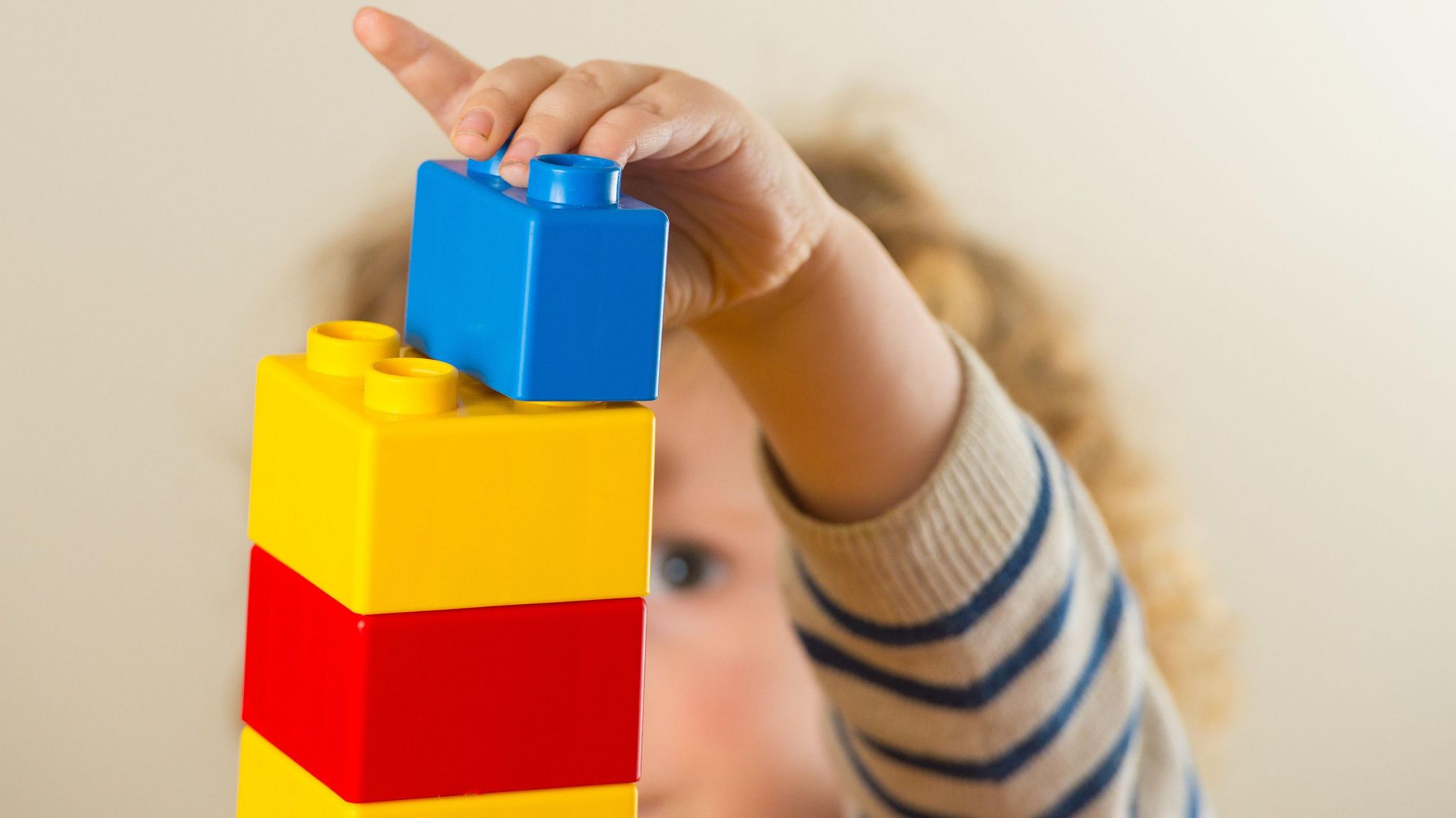 A toddler wearing a stripey jumper and blonde curly hair playing with building blocks