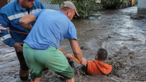 Two men pulling another man from floodwater, using rope