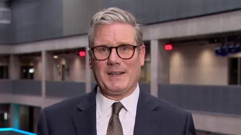 Labour leader Sir Keir Starmer wearing glasses, a blue suit and a brown tie on a white shirt