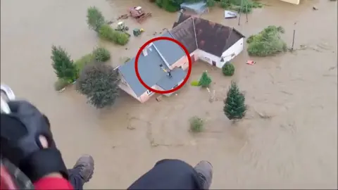 Circle around a man standing on a roof surrounded by flood water waiting to be rescued