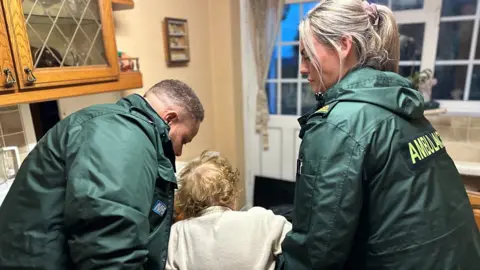 Two paramedics help an elderly woman off the floor
