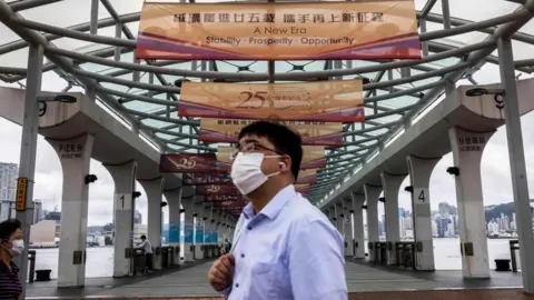 Getty Images A man walks past banners at a ferry pier with a slogan celebrating the upcoming 25th anniversary of Hong Kong's handover from Britain to China, in Hong Kong on June 16, 2022.