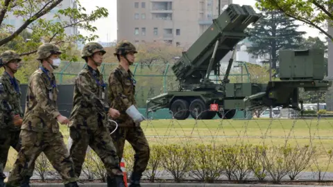 Getty Images Officers of Japan's Self-Defense Force walk in front of Patriot surface-to-air missile launchers.