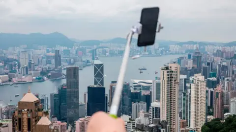 Getty Images A tourist holds a selfie stick (C) from the peak which overlooks the city of Hong Kong and Victoria Harbour on June 9, 2018