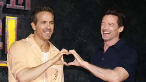 Getty Images Ryan Reynolds and Hugh Jackman form a heart with their hands at the Deadpool premiere