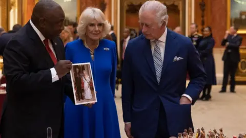 Getty Images Mr Ramaphosa holds a picture of Queen Elizabeth II with Nelson Mandela as he talks to Camilla and King Charles III.