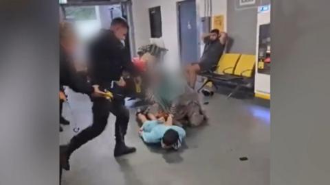 A police officer lifts his foot towards the head of a man who is lying on the floor