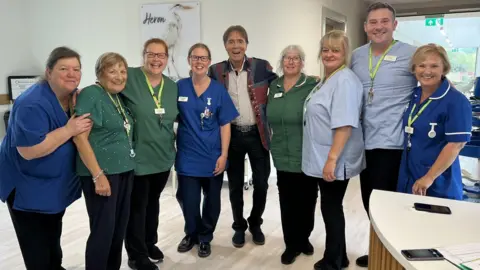 Sir Cliff poses with the hospice's clinical team for a group photo. He's wearing his Union Jack jacket. 