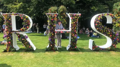 A woman poses with a floral RHS sign at Tatton Park