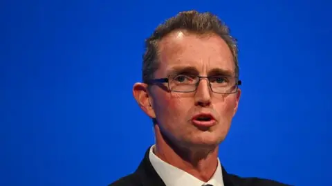 David TC Davies in front of a blue background