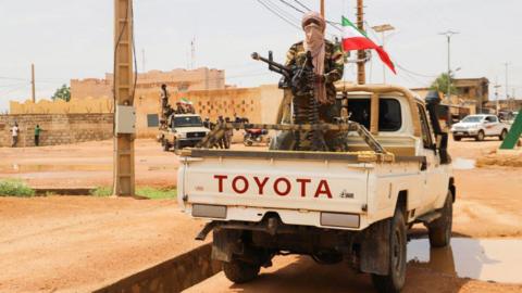 A Tuareg fighter on the back of a truck, standing next to a heavy machine gun