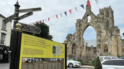 A picture of a street sign outside Howden Minster, pointing right to the toilets and post office, and pointing straight ahead to Corn Market Hill and the health centre