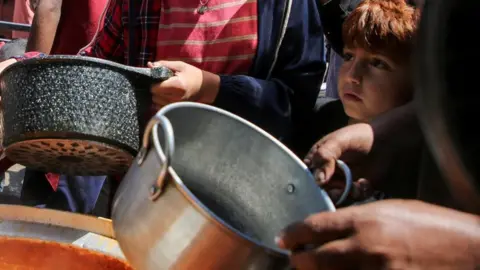 Reuters A young boy stands among a crowd holding bowls at an aid kitchen
