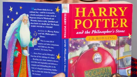 Close up of a man holding an early edition of the first Harry Potter book in front of his face