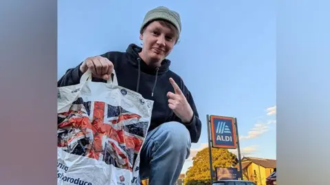 PA Media Leroy Lupton kneeling down with Aldi bag of shopping outside an Aldi store 