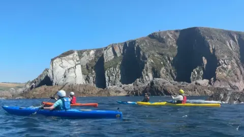 BBC Four kayakers in the sea in front of cliffs