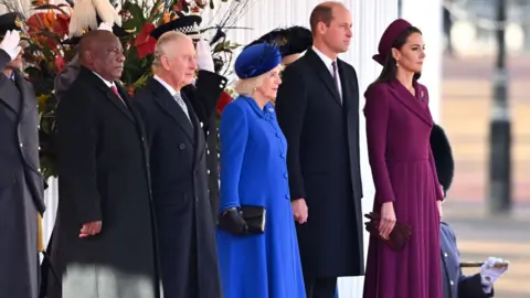 Getty Images Standing in a line from right to left with soldiers saluting behind them: Cyril Ramaphosa, King Charles, Queen Consort Camilla, Prince William, Princess Kate.