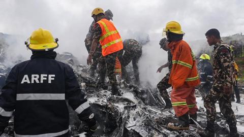 Rescue teams in hard hats and reflective vests work at the site of the crash in Kathmandu on 24 July