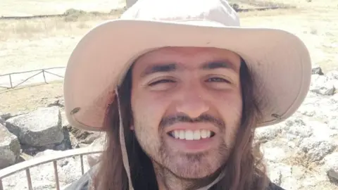 A man wearing a cream coloured sun hat smiles into the camera