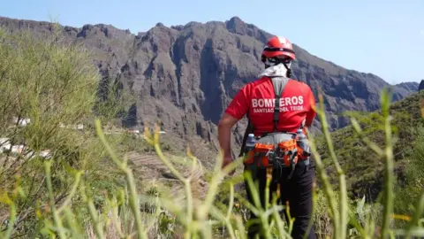 PA Media A firefighter searing near the village of Masca in northern Tenerife, a steep mountainside is visible in the bacground