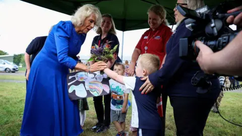 The Queen, wearing a long blue dress, was given a bunch of flowers from local nursery school children during her visit to RAF Leeming