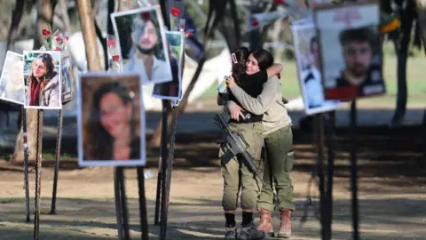 EPA Israeli soldiers hug as they look at pictures of the Nova music festival victims at the site of the festival near Kibbutz Reim