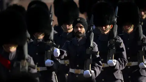 Getty Images Soldiers dressed in dark clothing march along with guns in hands.