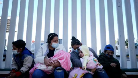 Getty Images El Salvador and Honduras nationals seeking asylum in the United States sit outside the El Chaparral border crossing on February 19, 2021 in Tijuana, Mexico